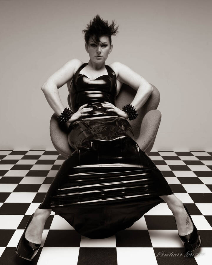 photographer Landicaa art fetish modelling photo. black latex dress brunette lady sitting on red chair.